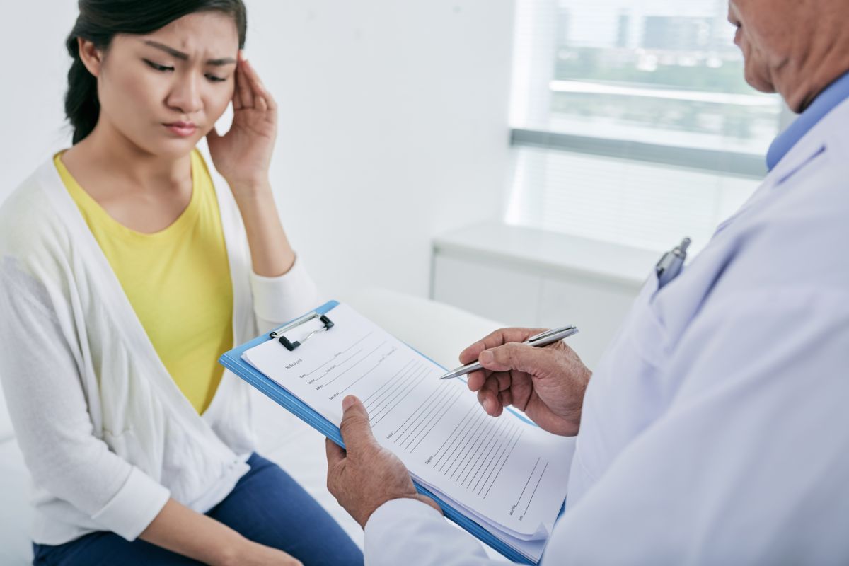 Young woman complaining about headache to her doctor