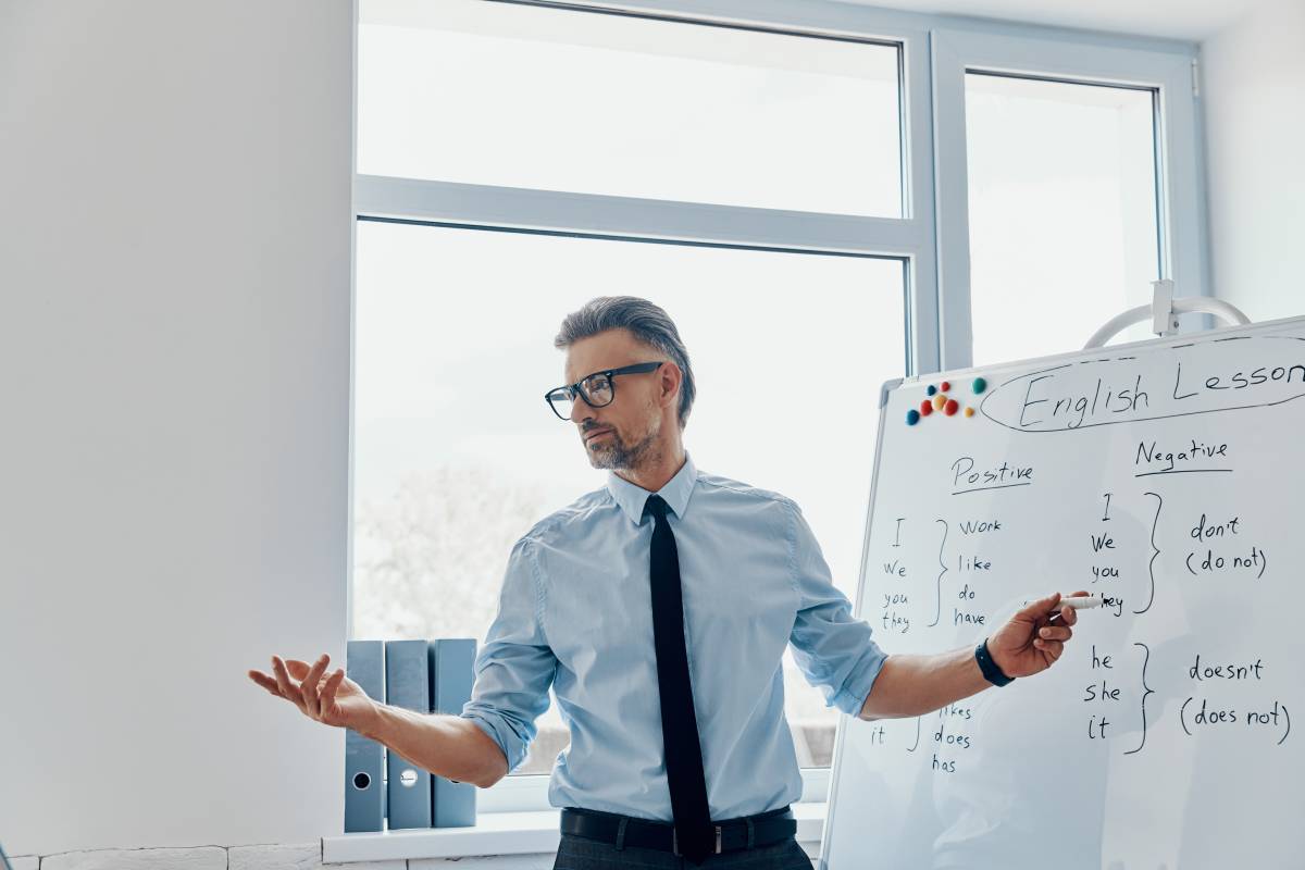 Confident English teacher pointing whiteboard while standing at the classroom