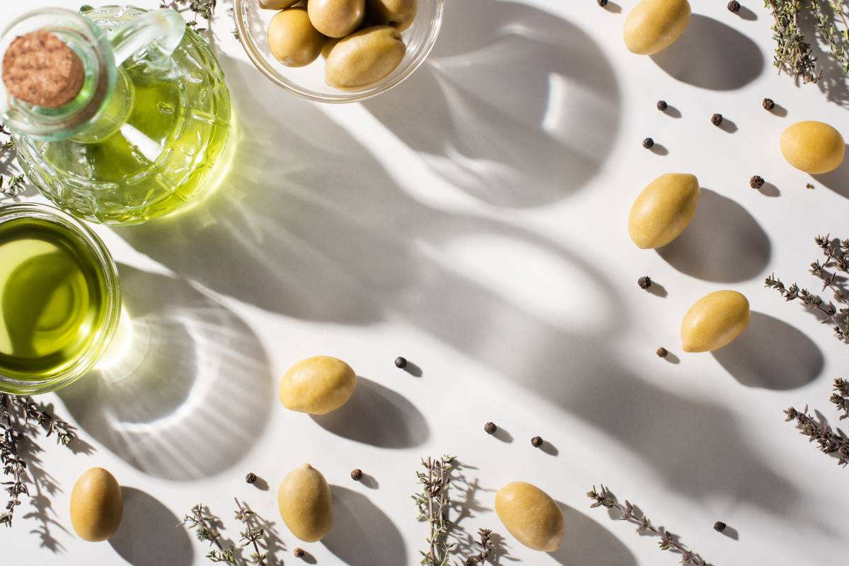 Olive Oil in Bottle And Bowl Near Herb, Green Olives And Black Pepper With Shadow