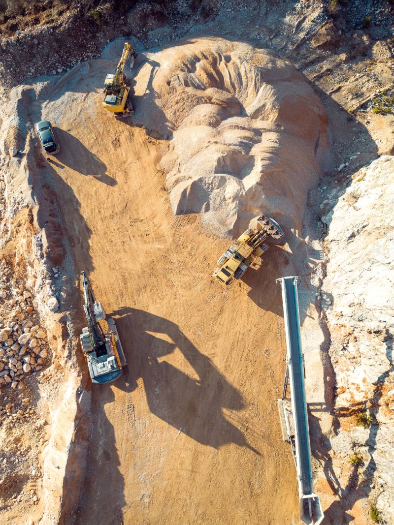 Aerial view of open pit quarry with heavy machinery working on the grounds. Excavators and trucks driving on the grounds. Sunny day in the countryside.
