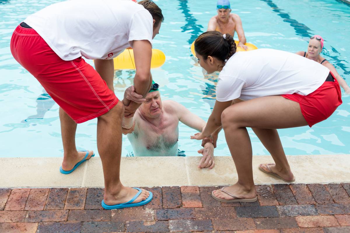 Male and female lifeguards helping Unconscious senior man in swimming pool
