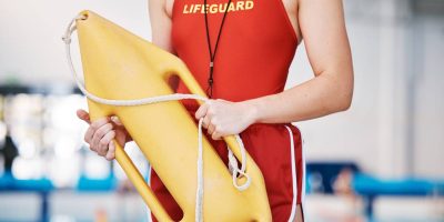 Swimming pool, hands of lifeguard with rescue tube and lifebuoy at water safety training exercise. .