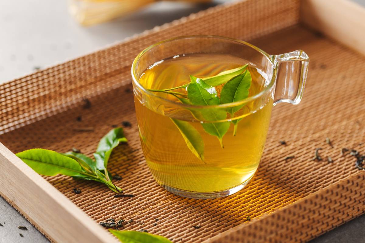 Green tea brewed in cup with tea leaves on table. Closeup.