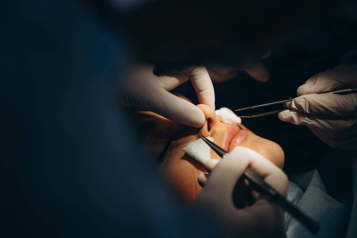 Surgeon and his assistant performing cosmetic surgery on nose in hospital operating room. Nose reshaping, augmentation. Rhinoplasty.