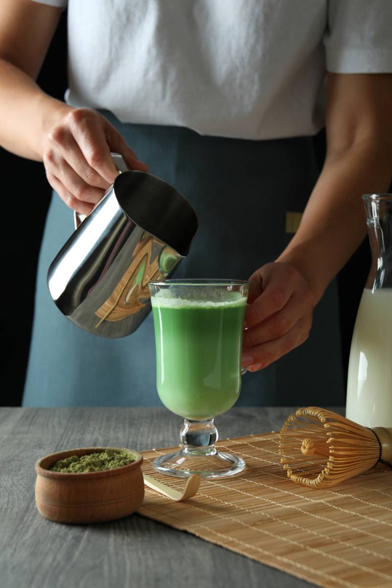 Woman making matcha latte on gray textured table