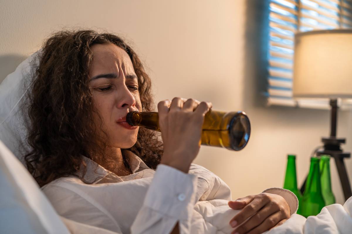 Drunk Latino woman hold beer bottle, and crying feel hangover on bed. Young beautiful depression female lying and crying in tears in bedroom, feel heart broken and celebrate life with alcohol at night