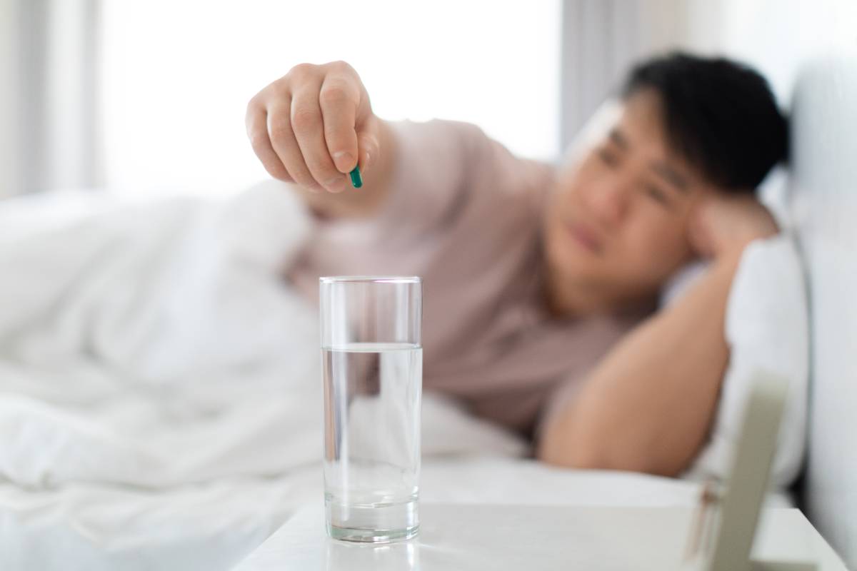 Glass of water on bed side table, man taking painkiller