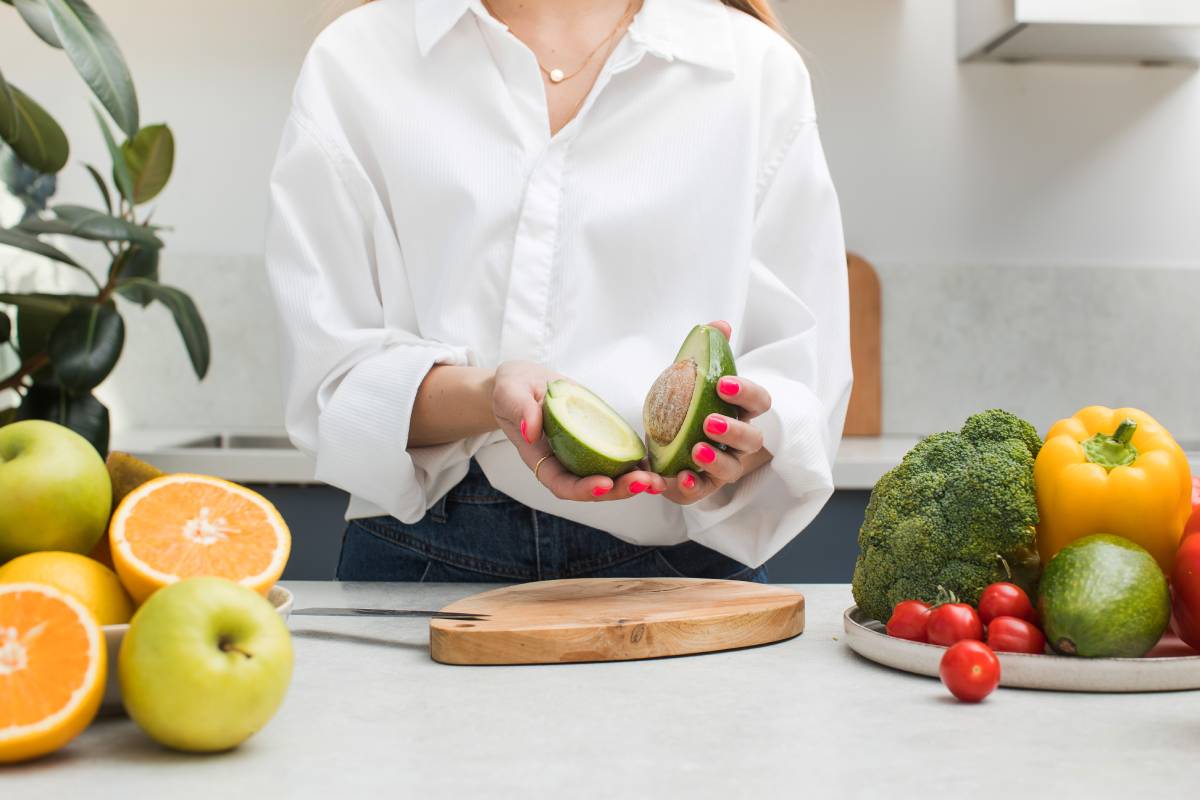 A woman cut a ripe avocado and holds two halves in her hands. Vegetarianism.