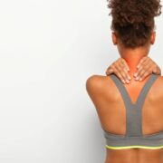Cropped image of faceless African American woman touches neck with both hands, shows problematic zone, being injured, dressed in active wear, poses over white studio wall, blank space for text