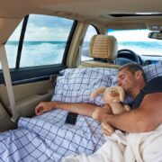 A young man sleeps in a hugging with a stuffed rabbit in the car by the ocean.