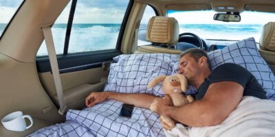 A young man sleeps in a hugging with a stuffed rabbit in the car by the ocean.