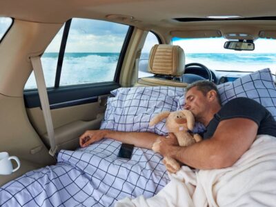 A young man sleeps in a hugging with a stuffed rabbit in the car by the ocean.