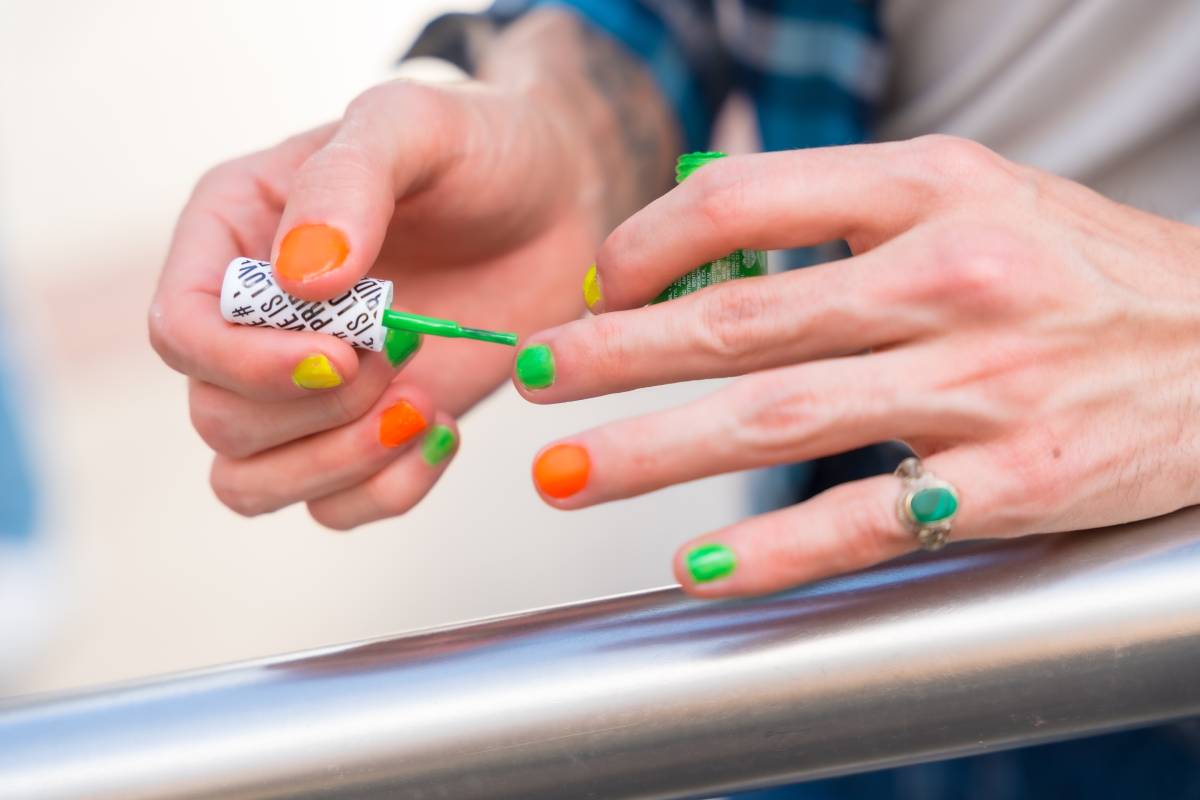 Attractive gay man painting his aviod nails makeup with rainbow lgbt flag in the city, pride party and homosexual