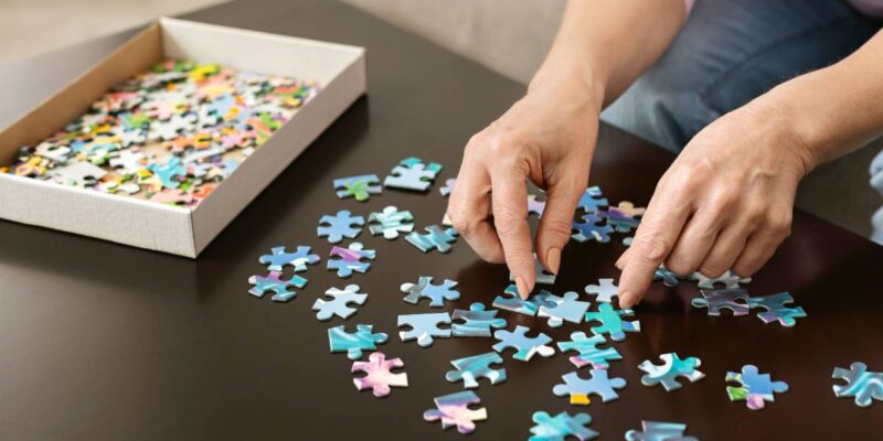 Elderly woman hands doing jigsaw puzzle closeup