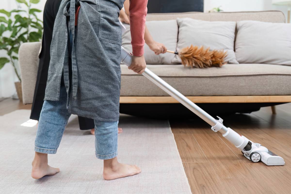 Home Cleaning and Teamwork. A young boy vacuums the floor while his mother assists with dusting.