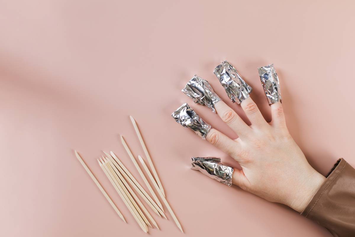 The process of removing long nails gel polish from nails. Nails are wrapped in falga on a pink background. Copy space.